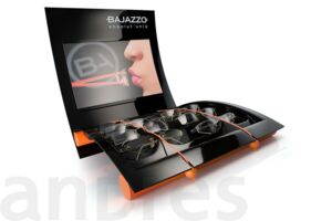 Thekendisplay für Bajazzo aus schwarzem tiefgezogenen Polystyrol. Das Logo wurde geprägt. Orangefarbene Kordeln, von Holzkugeln gehalten, sichern die exklusiven Markenartikel. Nahezu die gesamte Rückwand dient als Kommunikationsfläche.